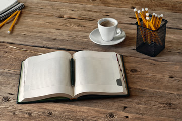 on the wooden table lies a open diary for entries with a cup of coffee and pencils. Top view. Copy space. Free space for text