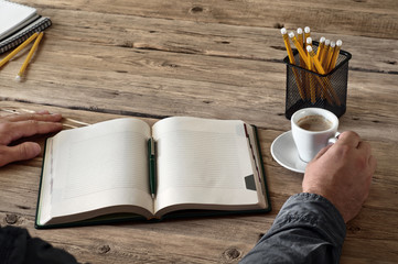 A man holding a cup of coffee over an open diary notes closeup. Top view. Free space for text. Copy space