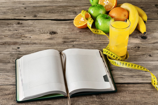 Open notebook for notes of fruit (apple, orange, banana) and orange juice on a wooden table. The concept of a healthy lifestyle and losing weight. Free space for text. Copy space. Top view