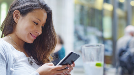 Attractive young woman sat at an outdoor cafe gently smiles as she looks at her phone