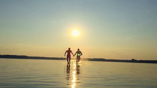 Two happy homosexual running on water at sunset