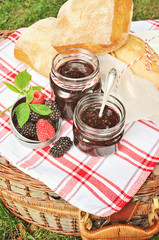 Fresh bread and blackberry jam in jars for picnic, toned image, selective focus