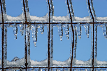 Ice Hanging From Wire Fence Against Blue