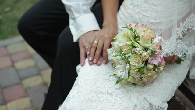 Bride caresses groom's hand near a bridal bouquet
