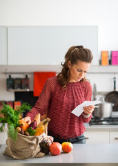 Woman in kitchen comparing shopping list to items in bag