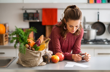 Woman in kitchen reading shopping list with shopping and receipt