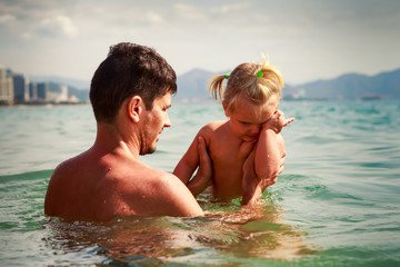 father holds little daughter in arms in sea water