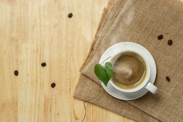 White cup of Espresso on brown burlap and heart leaves