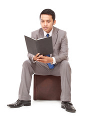 serious young businessman reading a book, isolated on white background