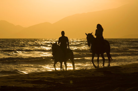 Horse rider couple at sunset beach, next to the sea