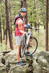 Young happy biker holding bike on a rock looking at camera