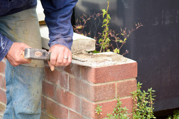 Bricklayer using lump hammer and bolster to clear old render off wall