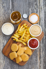 chicken nuggets with french fries, different sauces and a glass