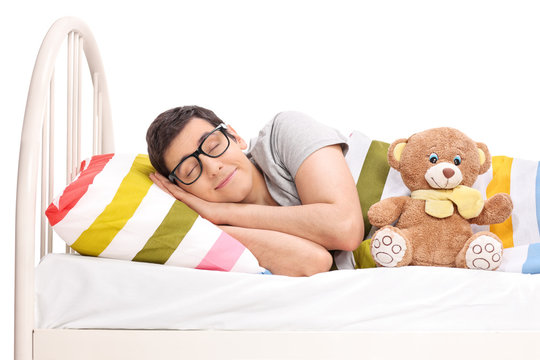 Joyful man sleeping in a bed with a teddy bear