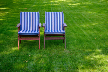 Two chairs with striped mattresses on a green grass