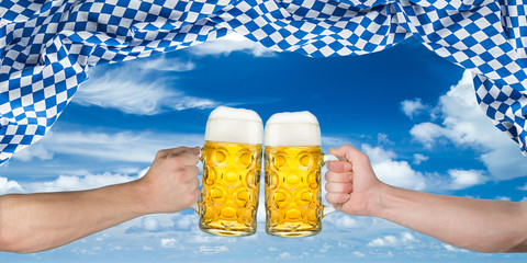 two hands holding beer mugs under bavarian flag in front of blue sky