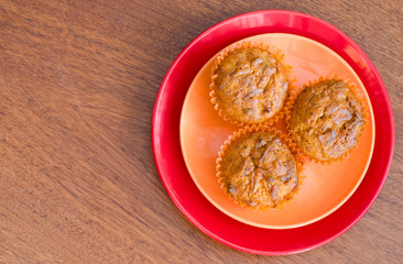 top view of three lemon muffins on an orange and red plate on a wooden table
