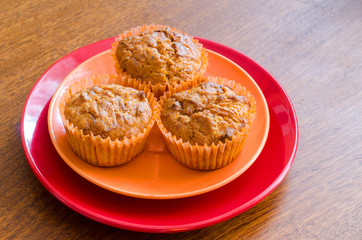 three lemon muffins on an orange and red plate on a wooden table