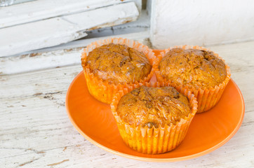 orange plate with three lemon muffins on an old white wooden window sill