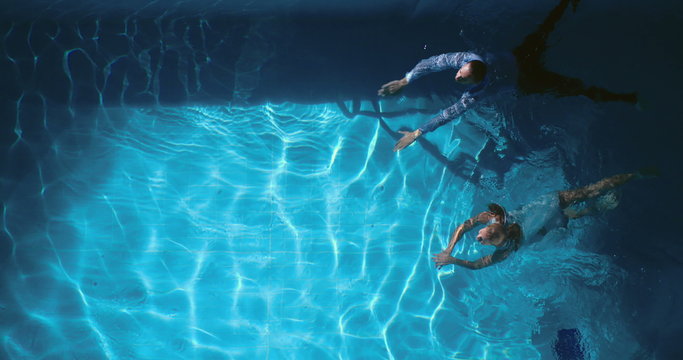 High angle view of couple in evening wear swimming across pool  