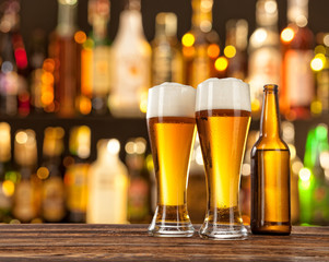 Glasses of light beer with bar on background