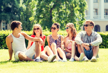 group of smiling friends outdoors sitting on grass