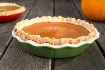 Freshly baked pumpkin pies cooling on rough wood boards. Green and red ceramic pie plates. Fresh pumpkin in the background. © colloidial