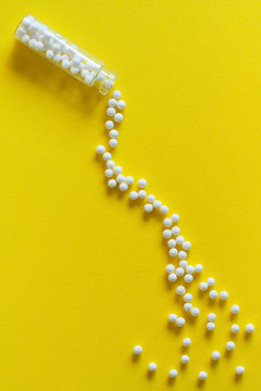 Homeopathic medicine spillage - Overhead view of homeopathic pills (made from inert substance - sugar/lactose) spillage effect from a bottle on a yellow surface. Natural light used.