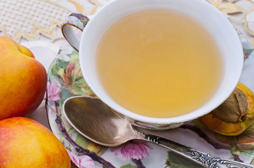 close-up of green tea in a vintage ornamental cup with metal spoon and fitting plate surrounded by peaches and nectarines