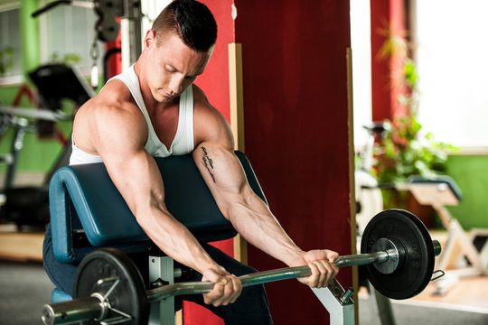 phisique fitness competitor works out in gym lifting dumbbells