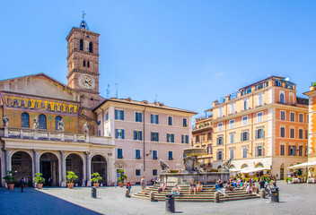 Fototapeta na wymiar people are strolling through piazza di santa maria situated in front of the basilica with the same name in trastevere district in rome.