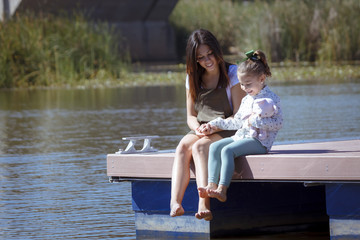 Madre e hija sentadas en el embarcadero. Una niña y su mama disfrutando del verano junto al rio....