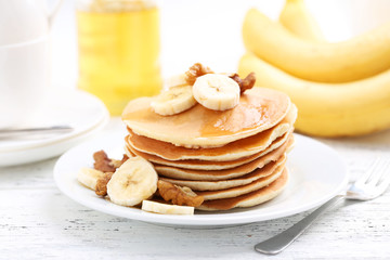 Tasty pancakes with banana and walnut on white wooden background