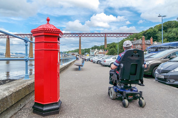 Fototapeta na wymiar Handicapped man in wheelchair passes red letterbox