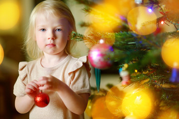 Fototapeta na wymiar Adorable little girl decorating a Christmas tree with colorful glass baubles at home
