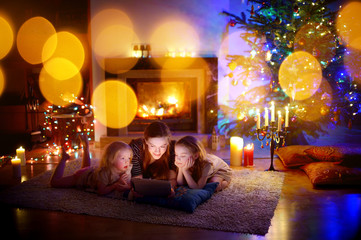 Mother and daughters using a tablet by a fireplace on Christmas