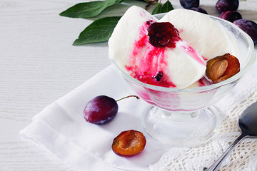 A bowl of ice cream with plum jelly and fresh plums on a white b