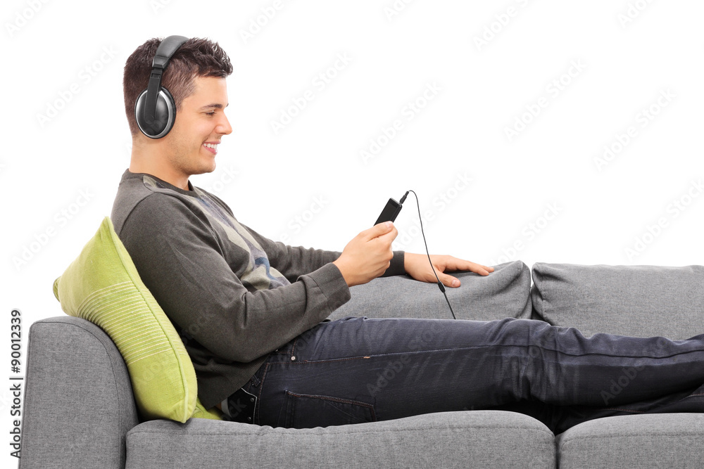 Sticker Young guy lying on sofa and listening to music on his phone