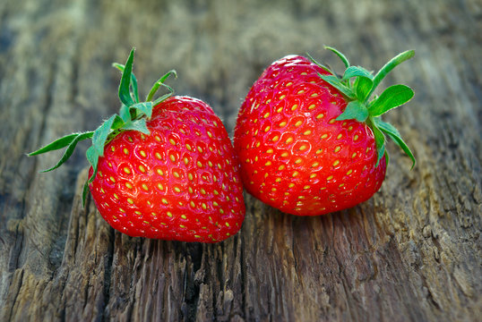 Two ripe strawberries on a wooden background