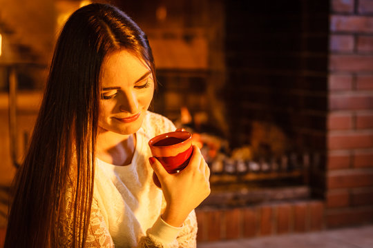 Woman drinking hot coffee relaxing at fireplace.