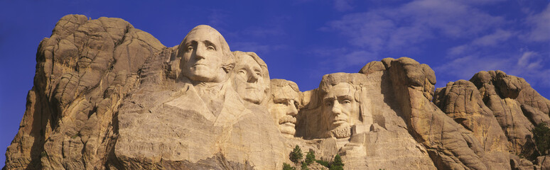 This is a close up view of Mount Rushmore National Monument against a blue sky. It shows the four faces of George Washington, Thomas Jefferson, Theodore Roosevelt, and Abraham Lincoln.