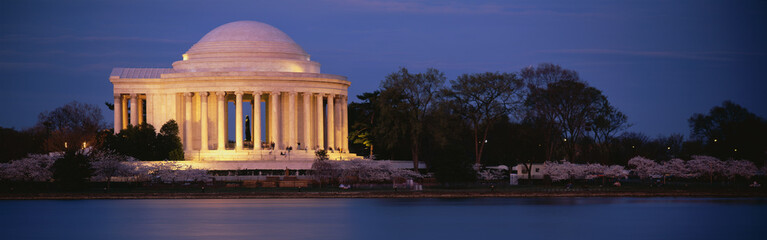 This is the Jefferson Memorial next to the Tidal Basin. Cherry blossoms are blooming on the trees surrounding it at dusk.