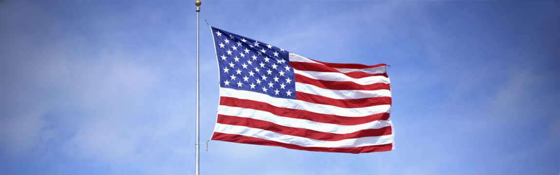 This is a shot of an American flag on a flagpole, waving in the wind against a blue sky.