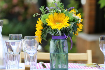 Objects: Sunflowers in a flower arrangement with a bow on a table with napkins, silverware and balloons in the background.