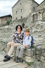 Obraz na płótnie Canvas The woman and boy sit on ancient blocks in Italy