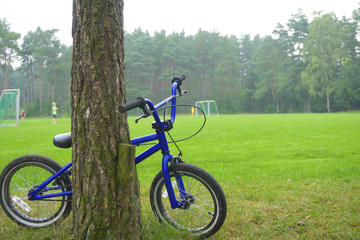 BMX - Fahrrad an einem Baum angelehnt, vor einem Bolzplatz auf dem Kinder spielen