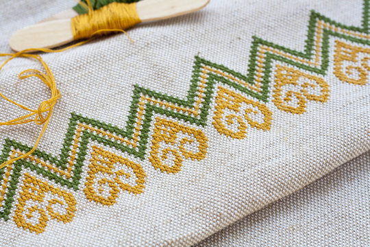 Ukrainian embroidery on the linen fabric and thread embroidery on a wooden table, selective focus