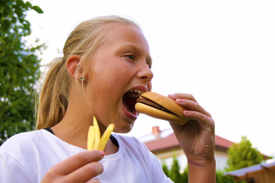 Blondes Mädchen isst draußen Hamburger und Pommes Frites.