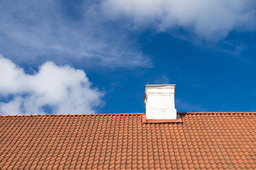 Typical tiled roof and white chimney against blue sky