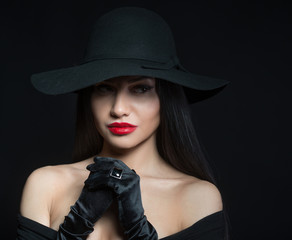 Woman in big black hat, studio portrait, dark background